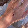 A woman's hand holding a Providence 3 Ruby vertical bar pendant featuring 3 petite baguette stones set in 14k yellow gold