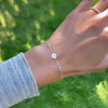 Woman's hand with a 14k gold Classic bracelet featuring birthstones and one 1/4” flat disc, engraved with a four leaf clover