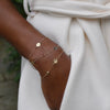 Woman wearing three 14k yellow gold cable chain bracelets featuring 1/4” flat discs engraved with letters