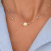 Woman with a 14k yellow gold Classic necklace featuring two birthstones and one 1/4” flat disc engraved with the letter H