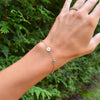 Woman's hand with a 14k yellow gold Classic bracelet featuring birthstones and one 1/4” flat disc engraved with the letter H