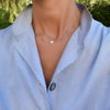 Woman wearing a 14k yellow gold Classic necklace featuring six birthstones and one 1/4” flat disc engraved with the letter H