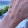 A woman's hand holding a Providence 5 Sapphire drop necklace featuring 5 petite baguette cut stones set in 14k yellow gold