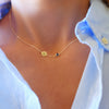Woman with a 14k yellow gold Classic necklace featuring one birthstone and one 1/4” flat disc engraved with the letter H
