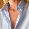 Woman wearing a 14k yellow gold Classic necklace featuring one birthstone and one 1/4” flat disc engraved with the letter H