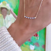 Woman's hand holding a Rosecliff bar necklace with eleven alternating 2 mm sapphires and diamonds prong set in 14k gold
