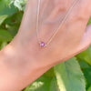 Woman holding a Grand 14k yellow gold 1.17 mm cable chain necklace featuring one 6 mm briolette cut bezel set pink sapphire