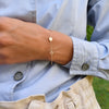 Woman wearing a 14k yellow gold cable chain bracelet featuring three 1/4” flat discs engraved with letters