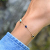 Woman's hand wearing a Grand 1.17 mm cable chain bracelet in 14k gold featuring four 4 mm and one 6 mm bezel set gemstones