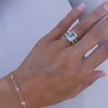 Braceleted woman's hand wearing a Warren ring in 14k gold with accent diamonds featuring one emerald cut Nantucket blue topaz