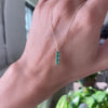 A woman's hand holding a Providence 3 Emerald vertical bar pendant featuring 3 petite baguette stones set in 14k yellow gold