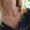 Woman wearing 2 necklaces including 14k gold necklace featuring birthstones and one 1/4” disc engraved with the female symbol