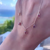A woman's hand holding a Providence 5 Garnet drop necklace featuring 5 petite baguette cut stones set in 14k yellow gold