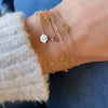Woman with a 14k gold Classic bracelet featuring two birthstones and one 1/4” flat disc engraved with a heart symbol