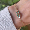 Woman with a 14k yellow gold Adelaide paperclip chain pavé bracelet featuring one emerald-encrusted link