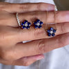 Hand holding a pair of Greenwich earrings and a necklace in 14k gold featuring 4 mm round cut sapphires and 2.1 mm diamonds