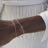 Woman wearing two bracelets including a Bayberry birthstone bracelet featuring 4 mm briolette amethysts bezel set in 14k gold