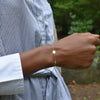 Woman wearing a 14k yellow gold Classic bracelet featuring one birthstone and one 1/4” flat disc engraved with the letter L