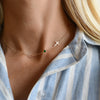 Woman wearing a 14k yellow gold 1.17 mm cable chain necklace featuring one round emerald and a 1/2