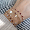 Woman with multiple bracelets including a De-Lovely cable chain bracelet featuring five birthstones bezel set in 14k gold