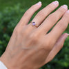 Hand wearing a 1.6 mm wide 14k yellow gold Grand ring featuring one 6 mm briolette cut bezel set amethyst