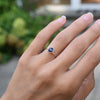 Woman's hand wearing a 1.6 mm wide 14k yellow gold Grand ring featuring one 6 mm briolette cut bezel set sapphire