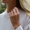Woman's hand wearing a 1.6 mm wide 14k yellow gold Grand ring featuring one 6 mm briolette cut bezel set pink opal
