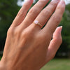 Hand wearing a 1.6 mm wide 14k yellow gold Grand ring featuring one 6 mm briolette cut bezel set pink opal