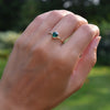 Hand wearing a 1.6 mm wide 14k yellow gold Grand ring featuring one 6 mm briolette cut bezel set emerald