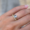 Hand wearing two rings including a 1.6 mm wide 14k gold Grand ring featuring one 6 mm briolette cut bezel set aquamarine