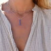 Woman wearing a Providence vertical bar pendant featuring 6 petite Sapphire baguette stones set in 14k yellow gold