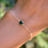Woman's hand wearing a Grand 1.17 mm cable chain bracelet in 14k gold featuring one 6 mm briolette cut bezel set emerald