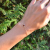 Woman's hand with a Grand 1.17 mm cable chain bracelet in 14k yellow gold featuring one 6 mm briolette cut bezel set garnet