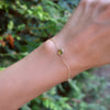 Woman's hand with a Grand 1.17 mm cable chain bracelet in 14k yellow gold featuring one 6 mm briolette cut bezel set peridot