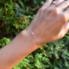 Woman's hand with a Grand 1.17 mm cable chain bracelet in 14k gold featuring one 6 mm briolette cut bezel set pink opal