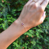 Woman's hand with a Grand 1.17 mm cable chain bracelet in 14k gold featuring one 6 mm briolette cut bezel set pink sapphire