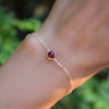 Woman's hand wearing a Grand 1.17 mm cable chain bracelet in 14k gold featuring one 6 mm briolette cut bezel set ruby