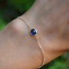 Woman's hand wearing a Grand 1.17 mm cable chain bracelet in 14k gold featuring one 6 mm briolette cut bezel set sapphire