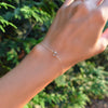 Woman's hand with a Grand 1.17 mm cable chain bracelet in 14k gold featuring one 6 mm briolette cut bezel set white topaz