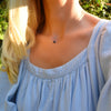 Woman wearing a Grand 14k yellow gold 1.17 mm cable chain necklace featuring one 6 mm briolette cut bezel set sapphire