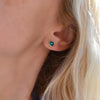 Woman's ear wearing a 14k yellow gold Grand stud earring featuring one 6 mm briolette cut bezel set emerald