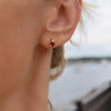 Woman wearing a 14k yellow gold Greenwich 1 Birthstone earring featuring one 4 mm garnet and one 2.1 mm diamond