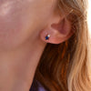 Woman wearing a 14k yellow gold Greenwich 1 Birthstone earring featuring one 4 mm sapphire and one 2.1 mm diamond