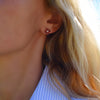 Woman wearing a 14k yellow gold Greenwich 4 Birthstone earring featuring four 4 mm garnets and one 2.1 mm diamond