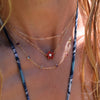 Woman wearing layered 14k gold necklaces including a Greenwich necklace featuring five 4 mm garnets and one 2.1 mm diamond
