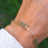 Woman wearing a 14k yellow gold Adelaide paperclip chain pavé bracelet featuring emerald-encrusted links