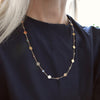 Woman wearing a 14k yellow gold Classic necklace featuring 10 birthstones and 10 flat discs engraved with letters 