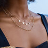 Woman wearing layered necklaces including a 14k gold necklace featuring four 1/4” flat engraved letter discs, spelling Mama