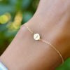 Woman's hand wearing a 14k yellow gold cable chain bracelet featuring one 1/4” flat disc engraved with the letter J