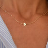 Woman with a 14k yellow gold cable chain necklace featuring one 1/4” flat disc engraved with the letter J